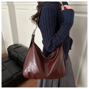 Détail du sac hobo en cuir marron foncé porté par un mannequin sur un mur de studio