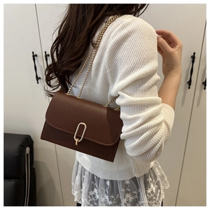 Détail d'un sac bandoulière en cuir marron avec boucle en U dorée et bandoulière chaîne