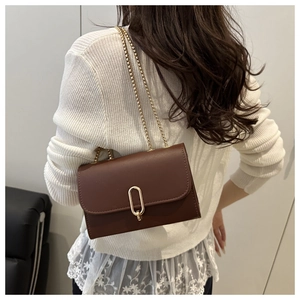 Detail der braunen Vintage-Ledertasche mit goldener Schnalle und Kette auf weißem Top