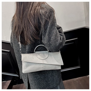 Detalle de bolso de mano en cuero gris con textura de cocodrilo y asa redonda plateada