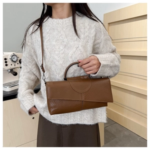 Bolso de mano marrón con textura de cocodrilo usado por una modelo en entorno doméstico