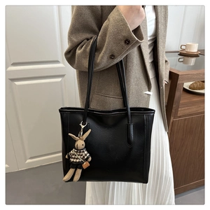 Detail of a black faux-leather tote bag featuring a cute bunny charm in a cozy indoor cafe