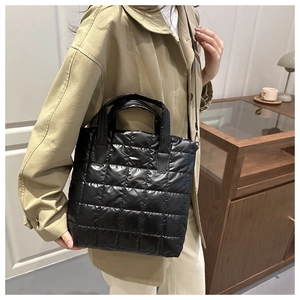 Detail of black quilted tote bag with shiny finish and shoulder strap in a cozy setting