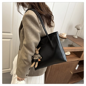 Detail of minimalist black PU leather tote bag with a checkered rabbit plush charm