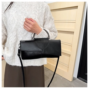 Detalle de bolso negro con relieve de serpiente y asa metálica llevado por una modelo