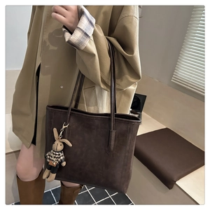Detail of dark brown leather tote bag with stylish rabbit charm and shoulder strap