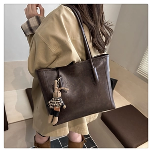 Detail of dark brown leather tote bag featuring a cute plush bunny charm on the side