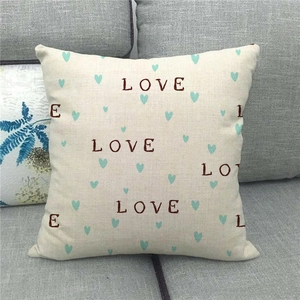 Close-up of linen pillow cover with brown Love typography and green hearts on sofa