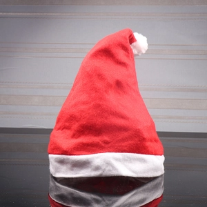 Close-up of a red felt Santa hat with white plush ball on a reflective dark surface