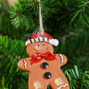 Macro detail of resin gingerbread man ornament with red bow on green Christmas tree branch