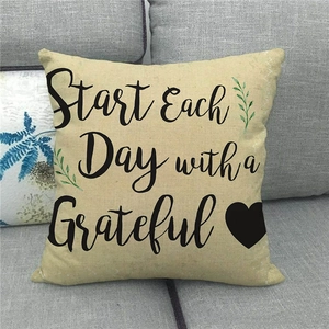Close-up of linen pillow cover with grateful quote and green leaf prints on sofa