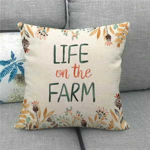 Close-up of linen pillow cover with floral wreath and 'Life on the Farm' text on sofa