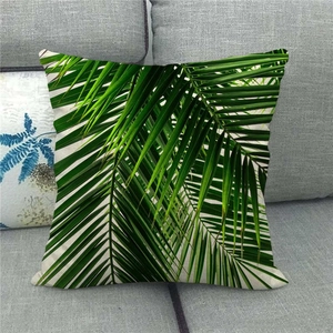 Detail of tropical green palm leaf pattern on linen pillow cover on a grey sofa