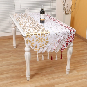 Christmas table runner with holly leaves and red tassels on white wooden table