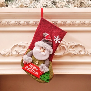 Large burlap Christmas stocking with Santa Claus doll and Merry Christmas tag by a fireplace