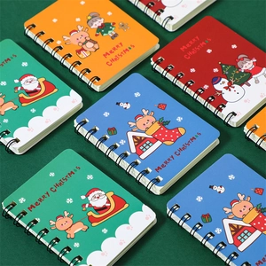 Close-up of Christmas mini spiral notebooks with festive illustrations on a green background
