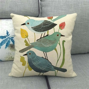 Detail of square linen pillowcase with cute blue bird and floral prints on a gray sofa