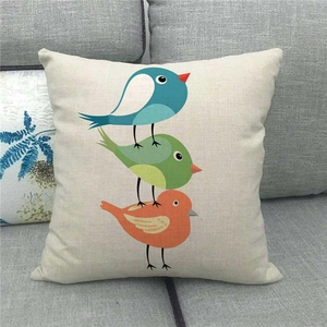 Close-up of linen pillowcase with three colorful cartoon birds on a gray sofa