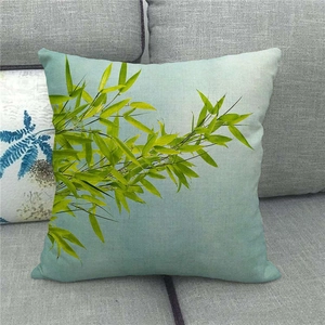 Detail of green bamboo leaf print on square linen pillowcase against grey sofa