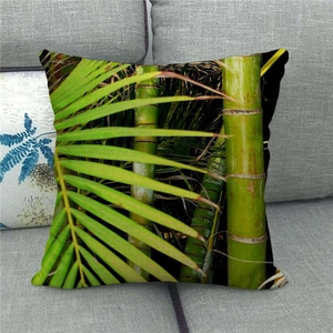 Close-up of green bamboo and palm leaf print on a linen pillowcase on a grey sofa