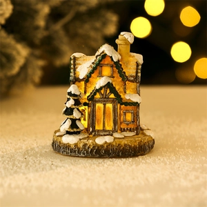 Close-up of glowing resin Christmas house with snowy roof and warm window lights