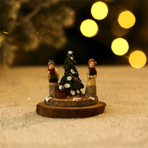 Close-up of miniature Christmas figures and snowy tree on wood base with bokeh lights