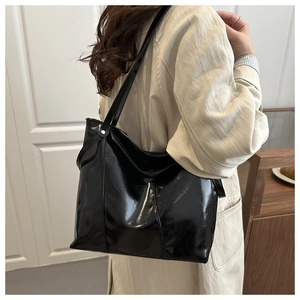 Detailed back view of a glossy black tote bag worn by a model in a minimal interior