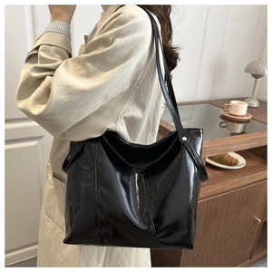 Detail of glossy black patent leather tote bag showing soft texture and long shoulder strap