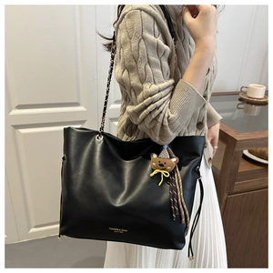 Detail of black faux leather tote with gold text and cute brown bear bag charm