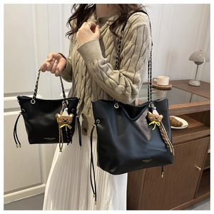 Detail of black leather bucket bag set with chain strap and cute brown teddy bear pendant
