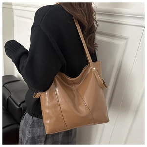 Close-up of the glossy brown tote bag material and stitching detail worn by a model