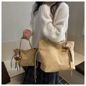 Detail of khaki suede tote bag set with golden chain strap and a cute bear charm