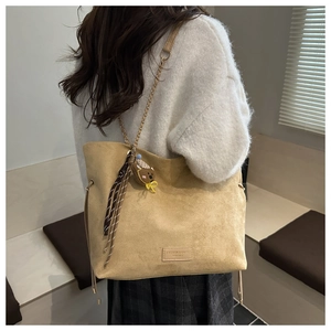Détail du sac cabas en daim moutarde avec chaîne en métal, ruban et breloque ours