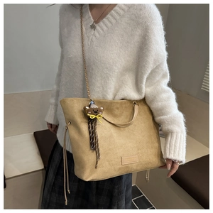 Detail of khaki suede tote bag featuring a cute bear charm and metal chain strap