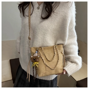 Détail du sac seau en daim kaki avec décor de chaîne et charmant pendentif ours