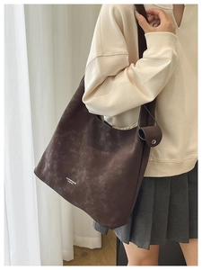 Détail d'un sac cabas en daim marron foncé avec logo blanc et texture mate