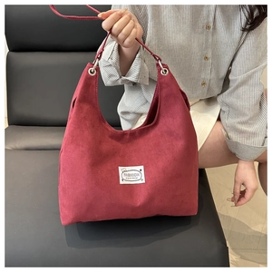 Detail of dark red suede hobo bag featuring white woven fashion label and metal eyelets