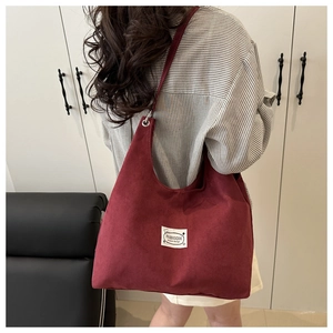 Detail of burgundy suede tote bag featuring fashion tag and spacious shoulder design