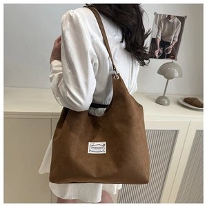 Close-up of brown suede tote bag featuring a teddy bear patch and stylish shoulder strap