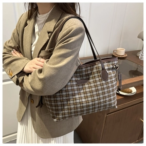 Detail view of plaid tote bag with brown leather straps and side drawstring on model