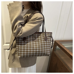 Detail of checkered tote bag featuring brown leather straps and tweed texture on shoulder