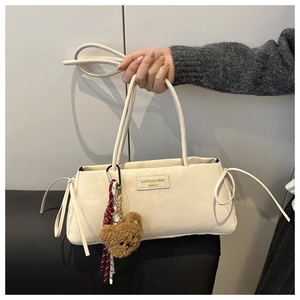 Detail of cream fabric shoulder bag featuring a mini plush bear charm and brand plaque