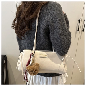 Detail of cream leather shoulder bag with plush bear charm and brand logo label