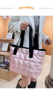 Detail of pink quilted tote bag with metallic finish and black strap on a wooden shelf