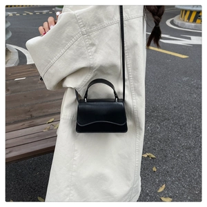 Street style shot of a black PU leather crossbody bag with wave edge and metal buckle
