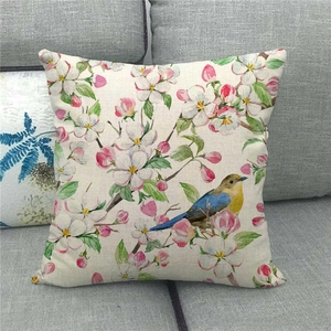 Linen cushion cover with watercolor flower and bird print on a cozy grey fabric sofa
