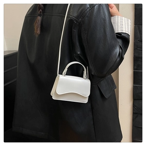 Détail du mini sac blanc à rabat ondulé porté sur un fond de veste en cuir noir