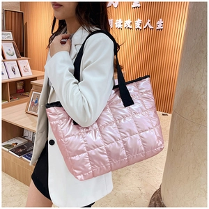 Pink quilted puffer tote bag with black strap worn by a model in a cozy setting