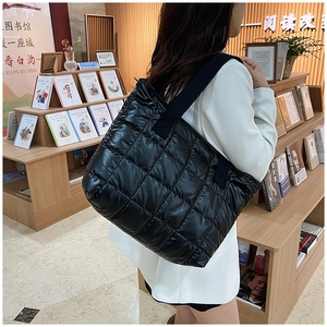 Detailed side view of black quilted puffer tote bag in glossy nylon on a female model