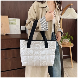Detail of white quilted tote bag with black straps and glossy nylon fabric texture